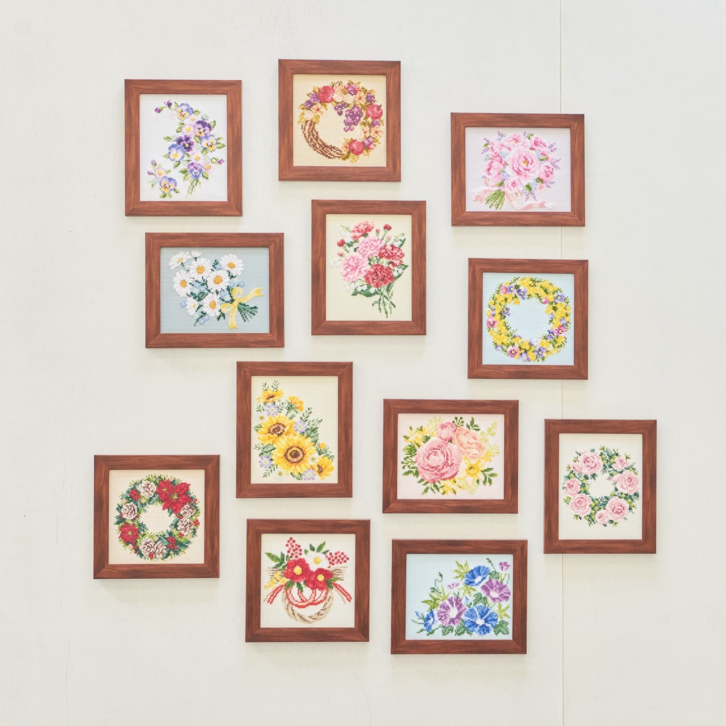 Twelve wood-framed floral embroidery pieces arranged as a gallery wall of wreaths and bouquets