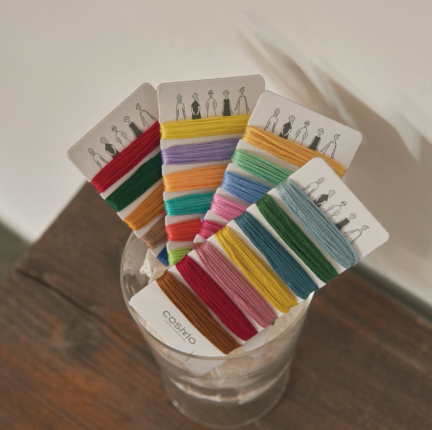 Hand-wrapped COSMO floss palette cards fanned in a clear glass jar on wood