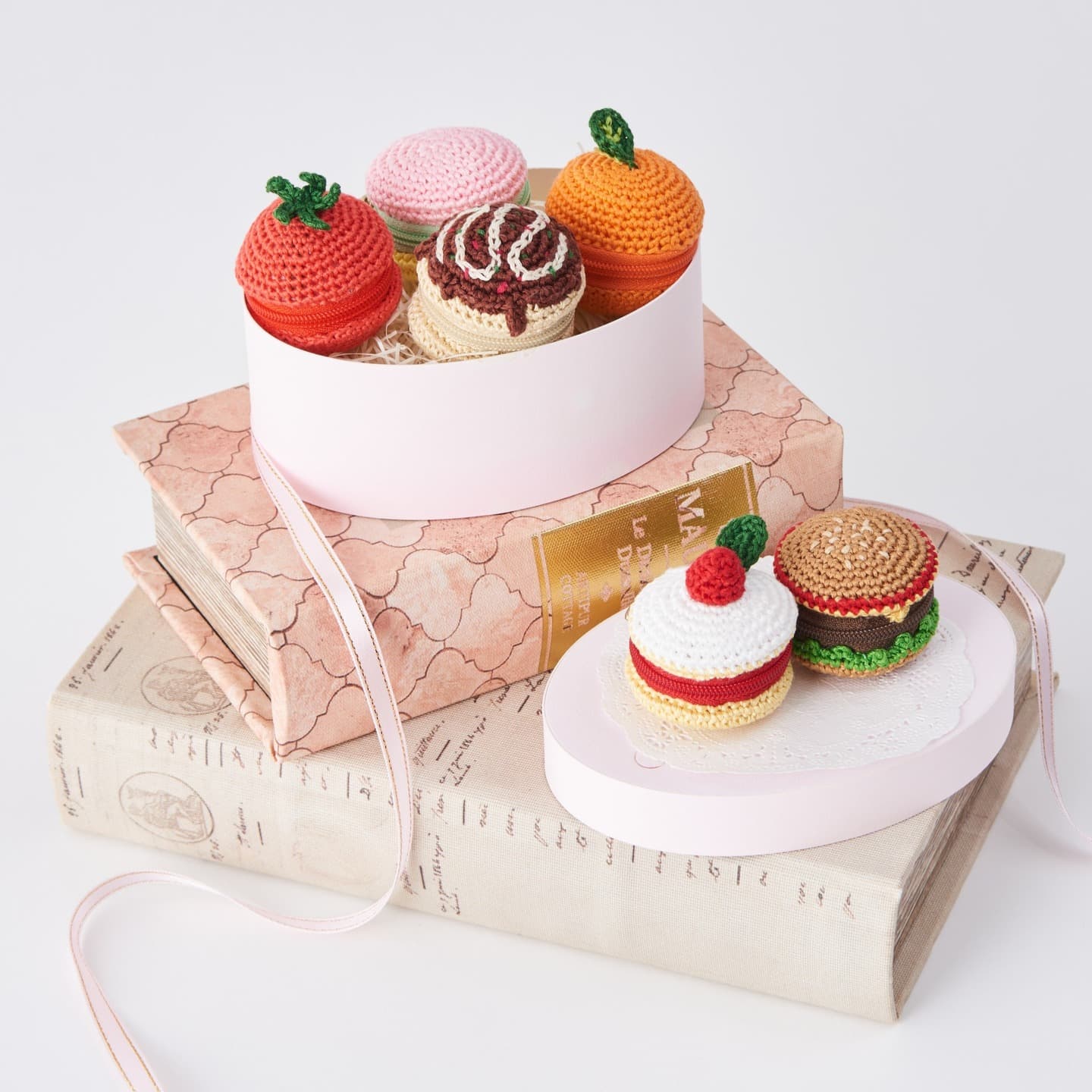 Six food-themed mini pouches crocheted with COSMO embroidery floss, arranged in pink boxes on vintage books