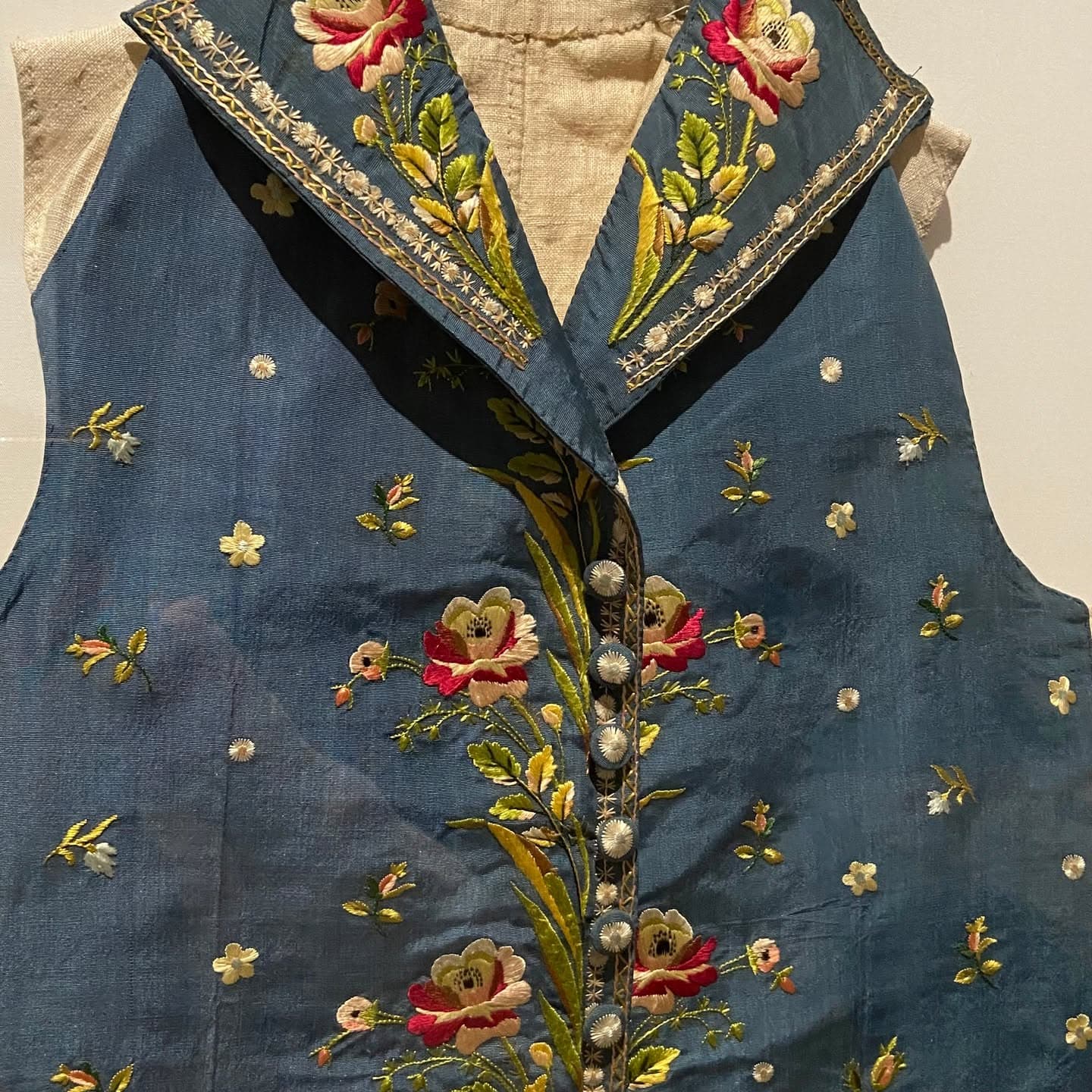 Close-up of a teal silk vest with dense rose and leaf embroidery along the lapels and button placket