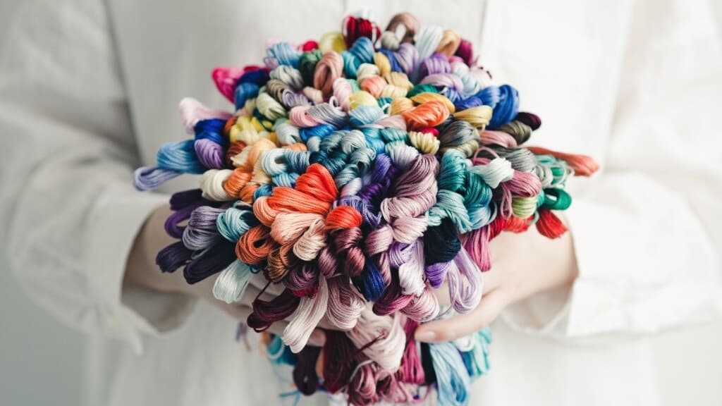 Hands holding a bouquet of multicolored COSMO embroidery floss skeins