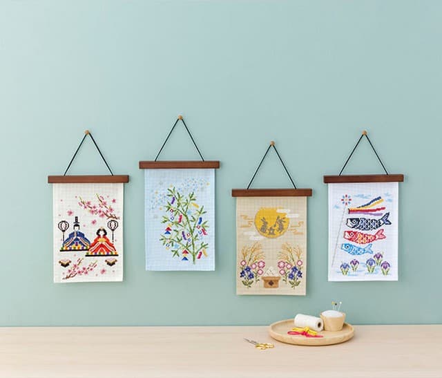 Four Japanese festival embroidery hangings—Hina dolls, Tanabata bamboo, Tsukimi moon rabbits, and koinobori—with floss and gold scissors on a wooden table