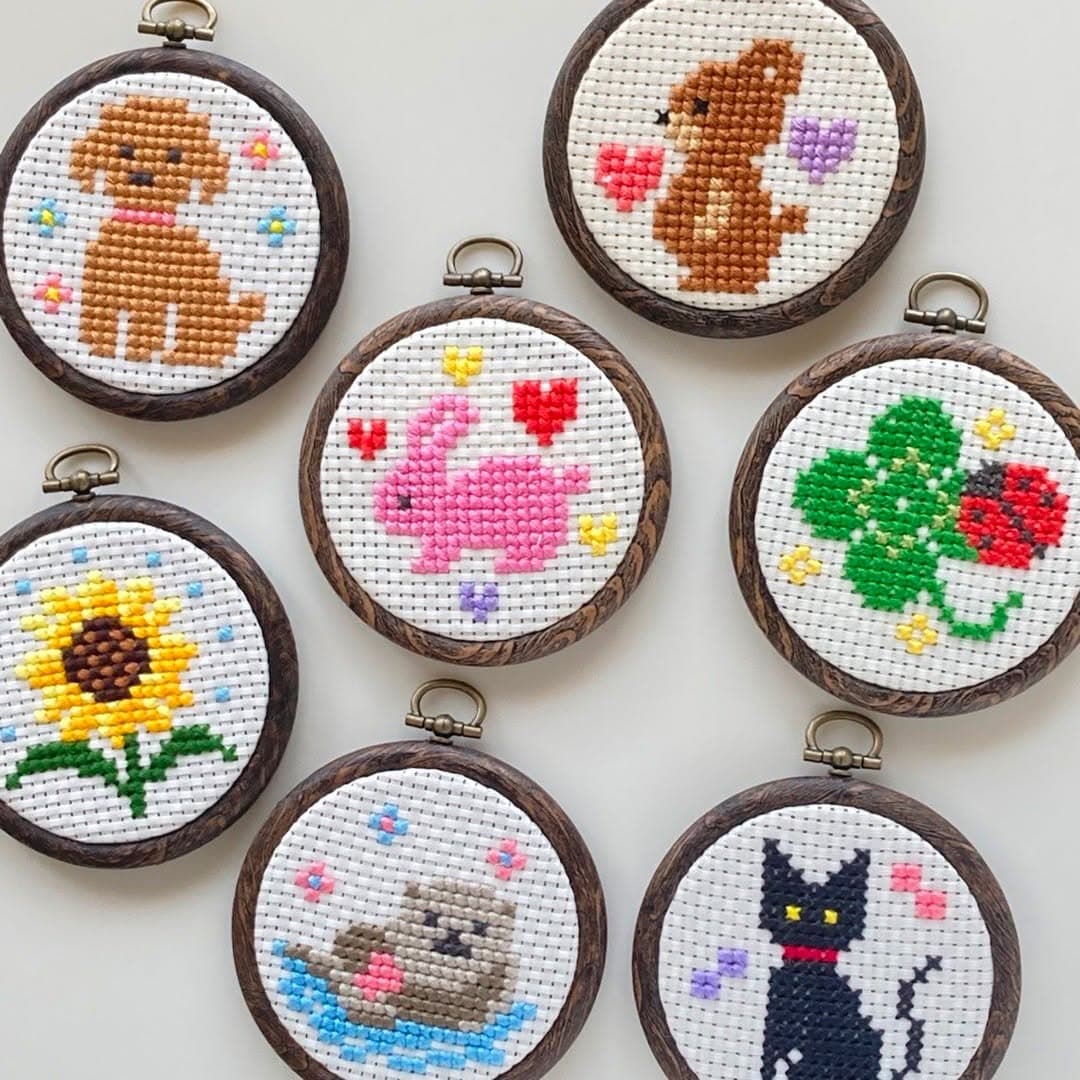 Seven miniature cross-stitch motifs in small wood hanging hoops on a white surface