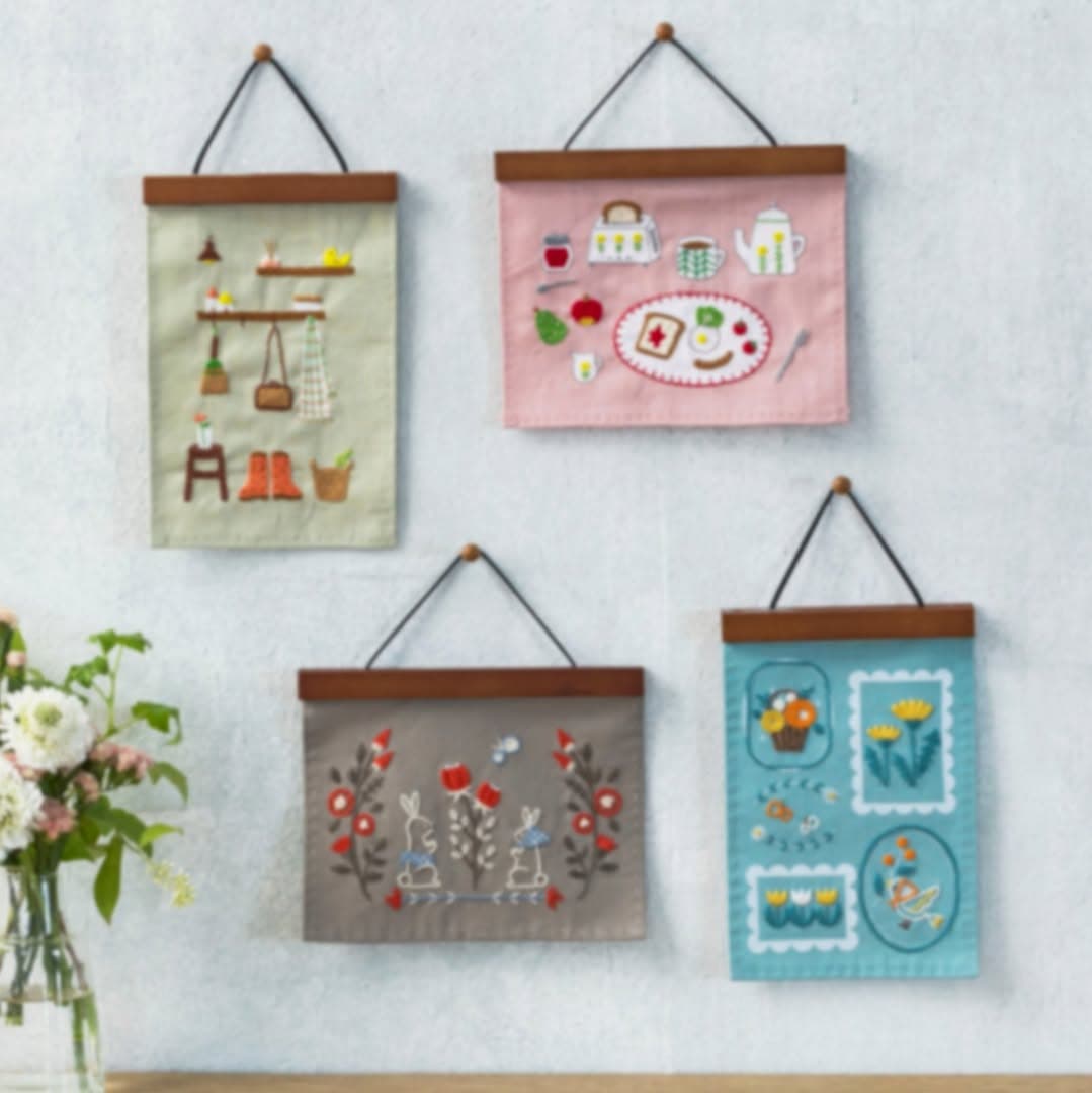Four folk-inspired embroidered wall hangings displayed on a textured white wall