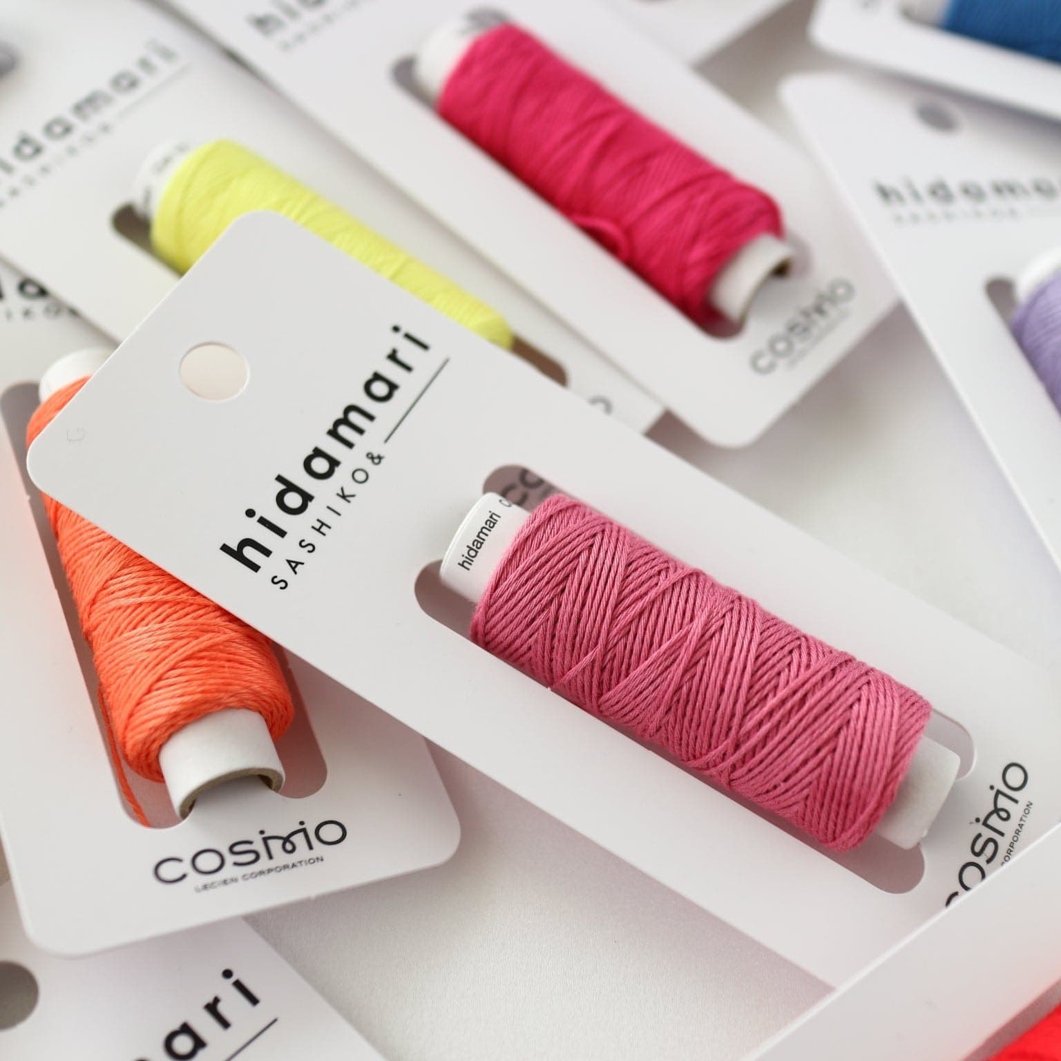 Close-up of colorful COSMO hidamari sashiko thread packs in pink, orange, and yellow
