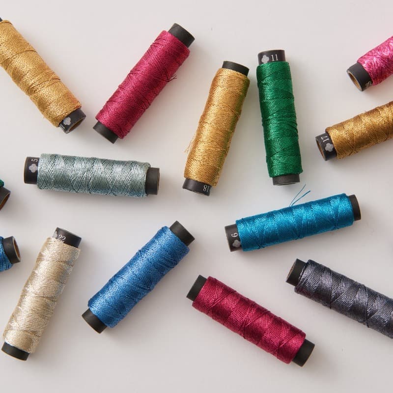 A scattered arrangement of colorful COSMO Nishikiito metallic thread spools in gold, magenta, teal, and green