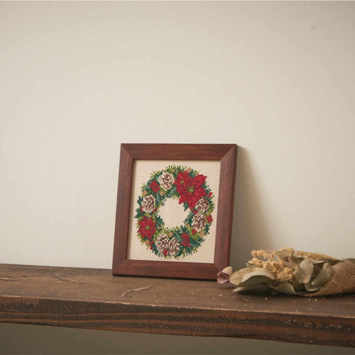 Framed winter poinsettia and pinecone wreath on a shelf with dried botanicals