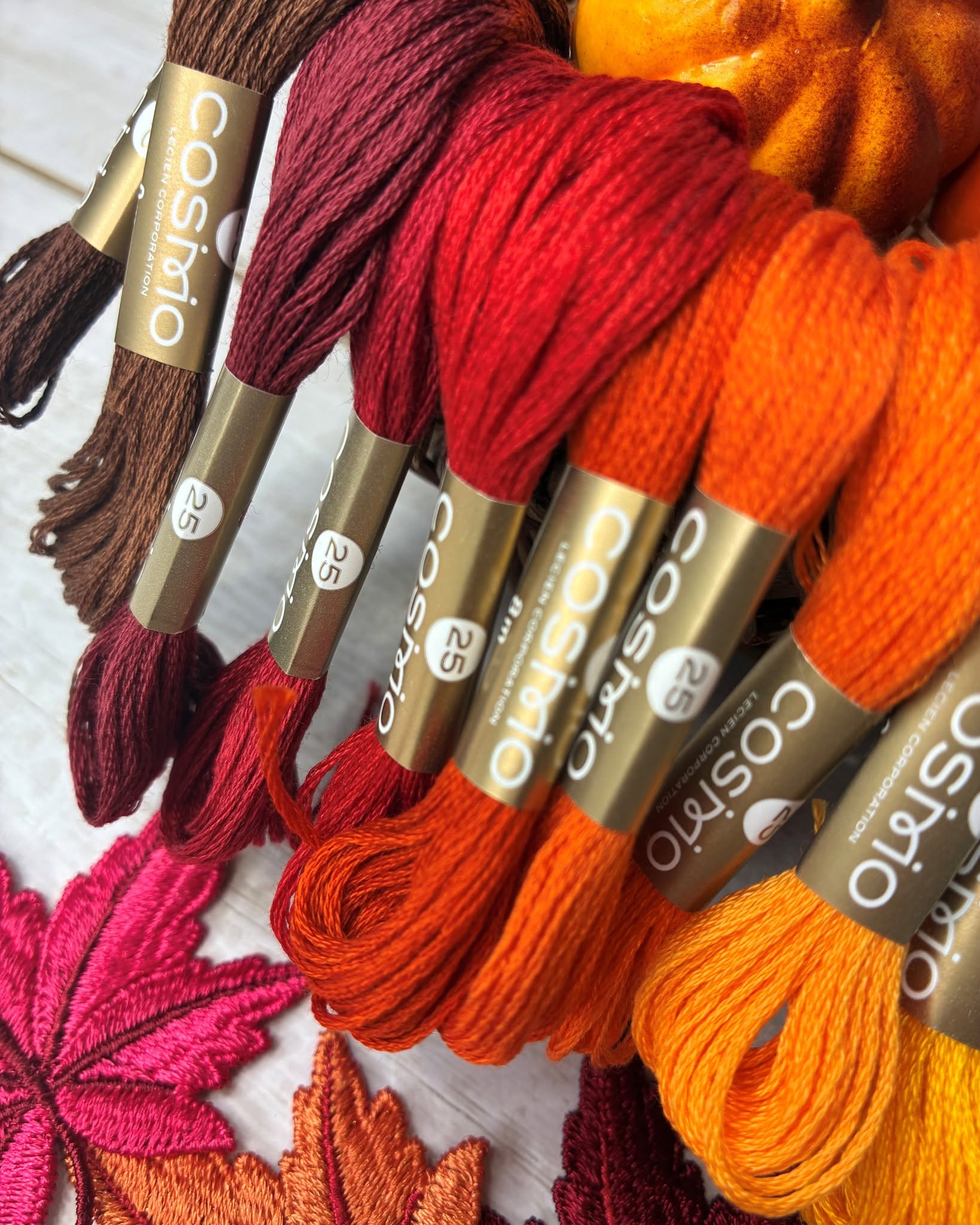 Autumn-toned COSMO Seasons and solid floss arranged with maple and pumpkin accents