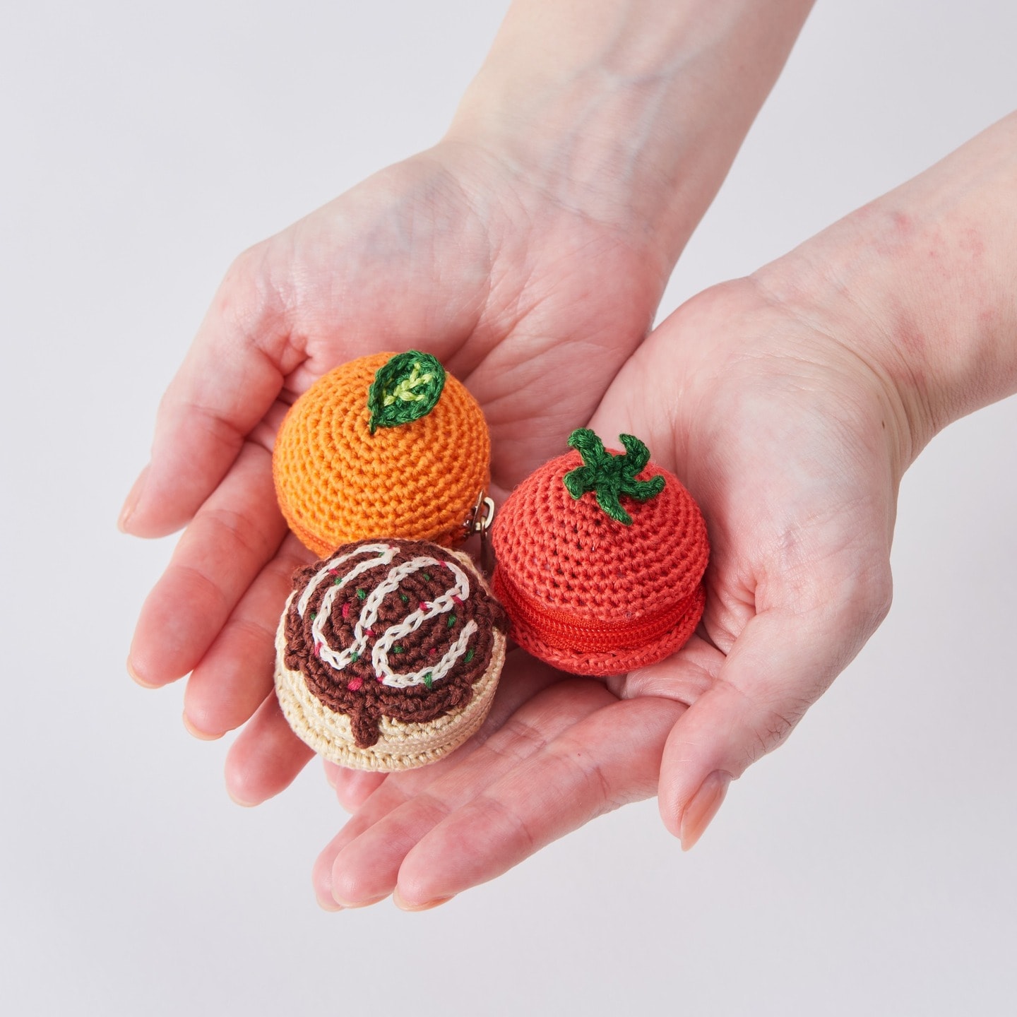 Tomato, orange, and chocolate pouches crocheted with COSMO embroidery floss, held in cupped hands