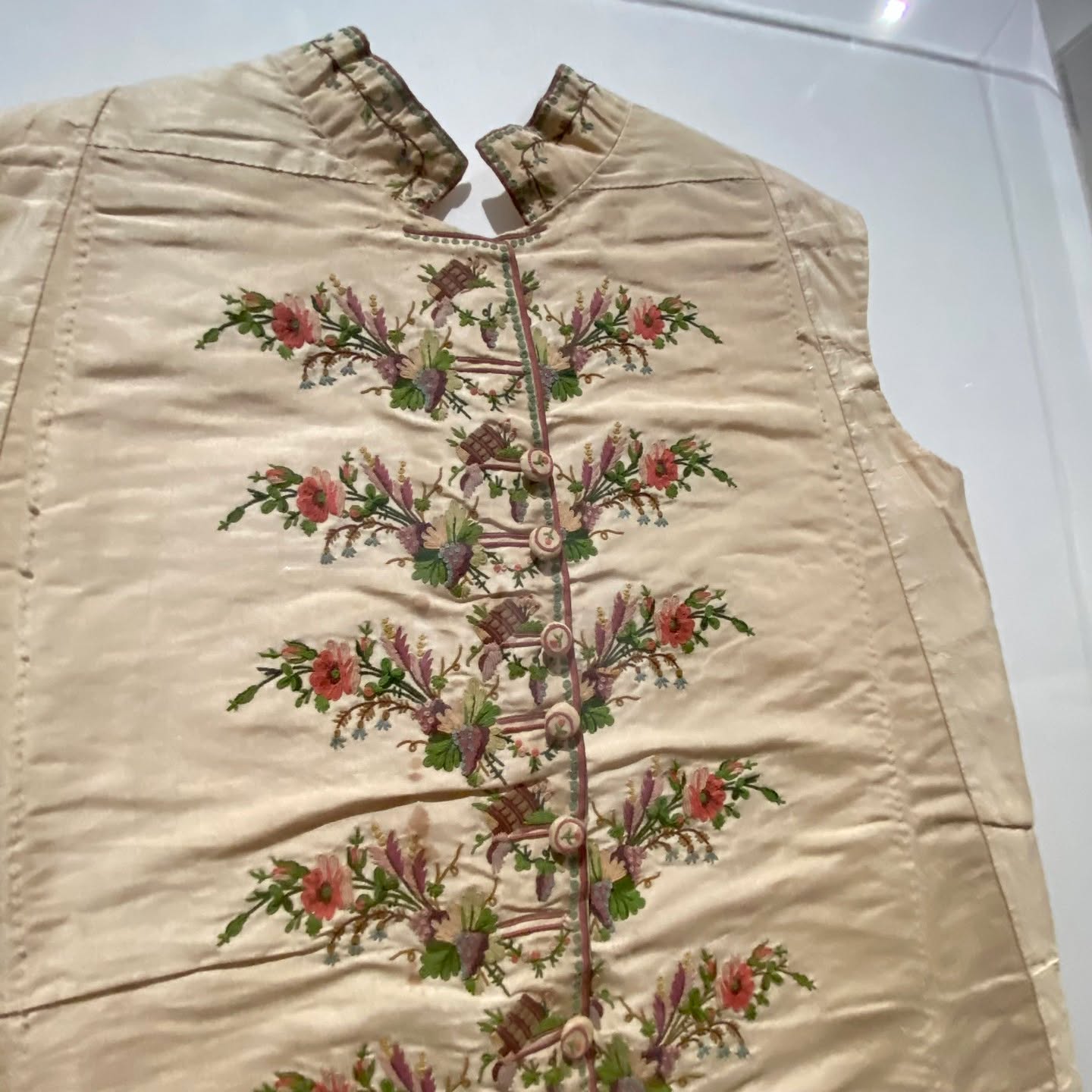 Cream silk waistcoat with horizontal floral sprays growing from a button placket, each rising from a tiny brown basket motif
