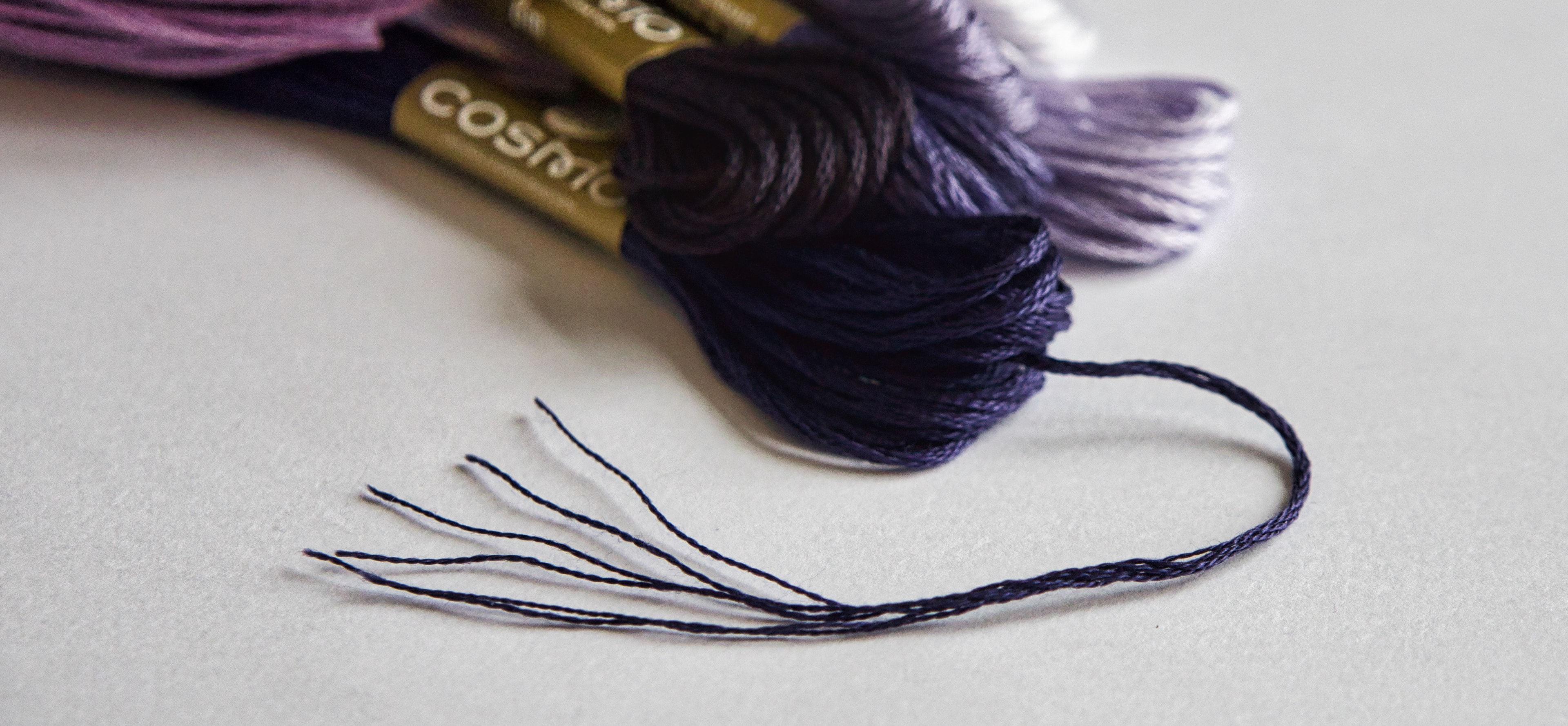 COSMO embroidery floss skeins in purple and navy with one strand separated into six plies