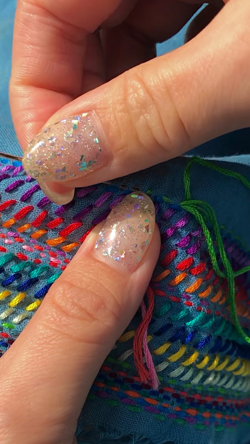 Close-up of hand stitching parallel rainbow running stitches on blue fabric