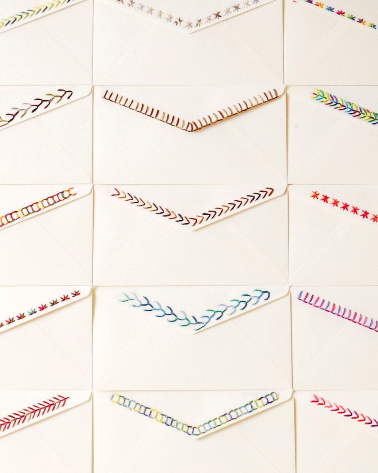 Grid of cream envelopes with different embroidered flap-edge stitch patterns in red, brown, and variegated colors