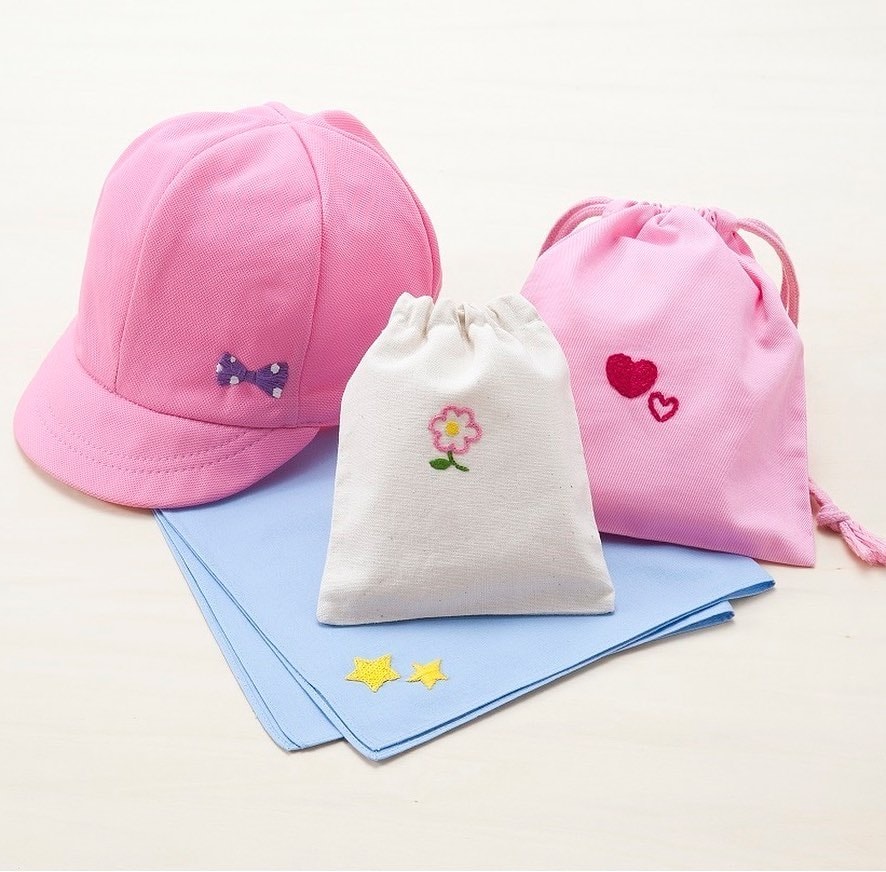 Pink cap with embroidered bow, white and pink drawstring bags with flower and heart motifs, and light blue cloths with yellow stars