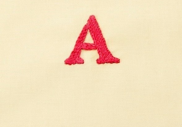 Finished magenta satin-stitch letter A on cream fabric