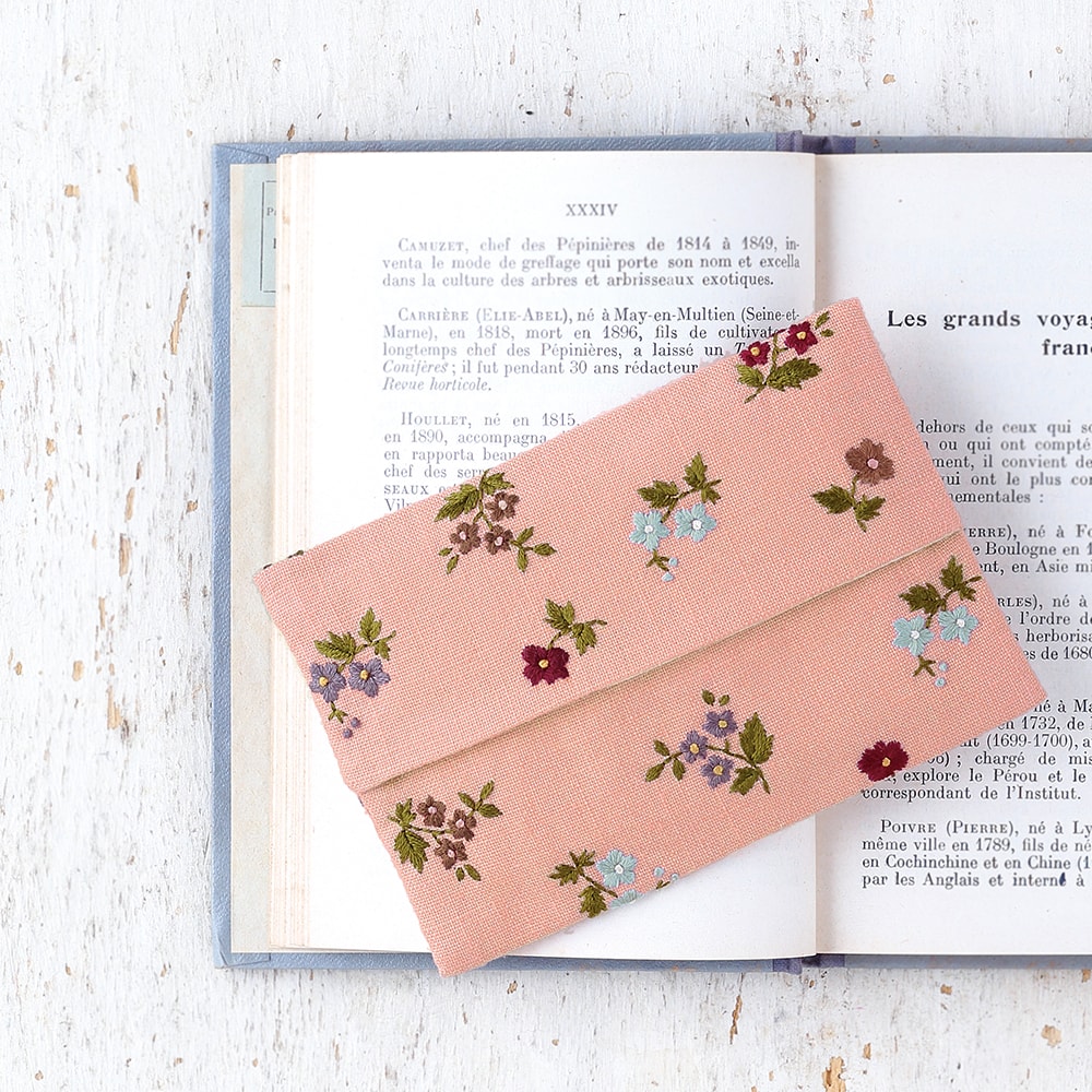 Dusty rose envelope pouch with scattered multi-color floral embroidery on an open vintage book