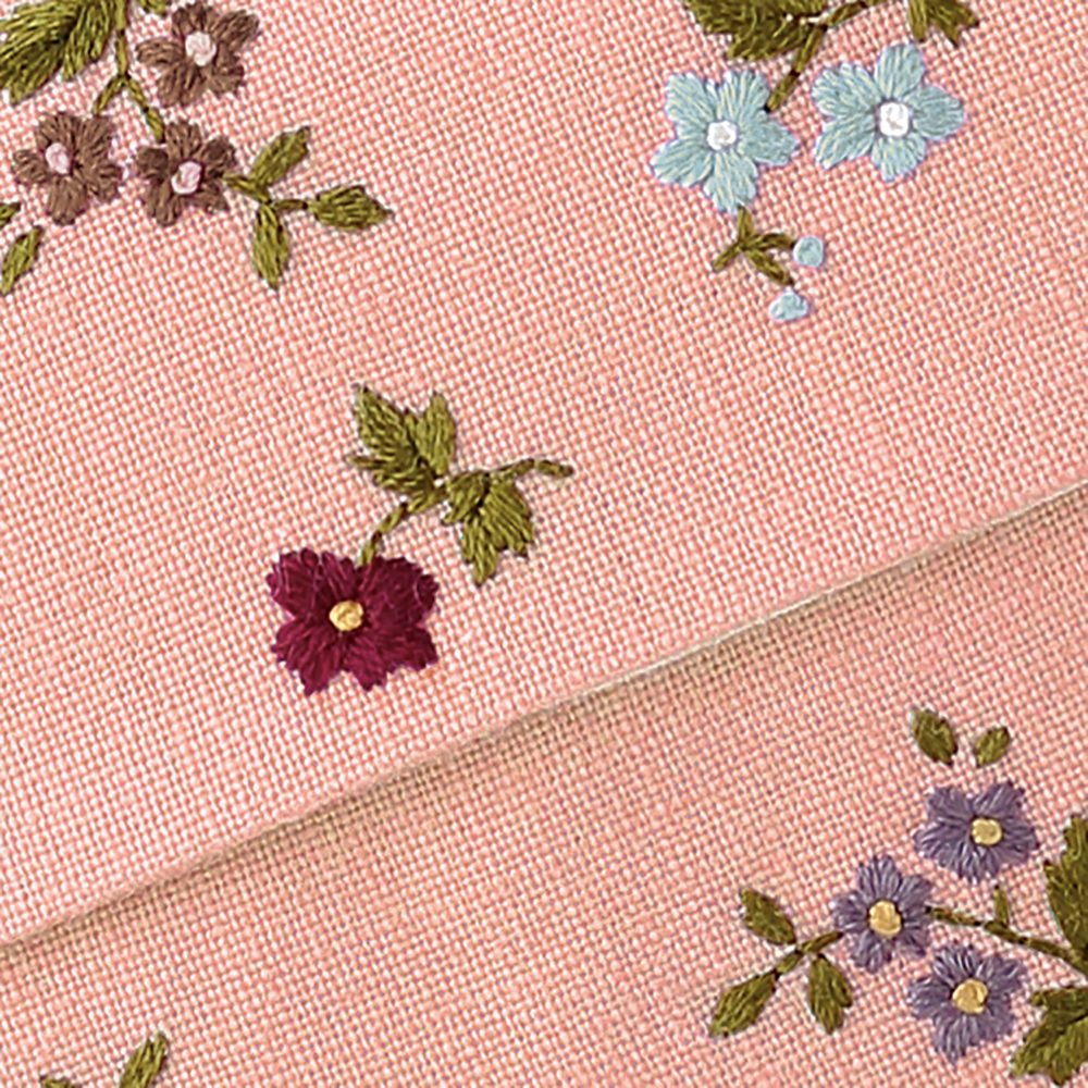 Close-up of small embroidered flowers in burgundy, blue, lavender, and brown on dusty rose fabric