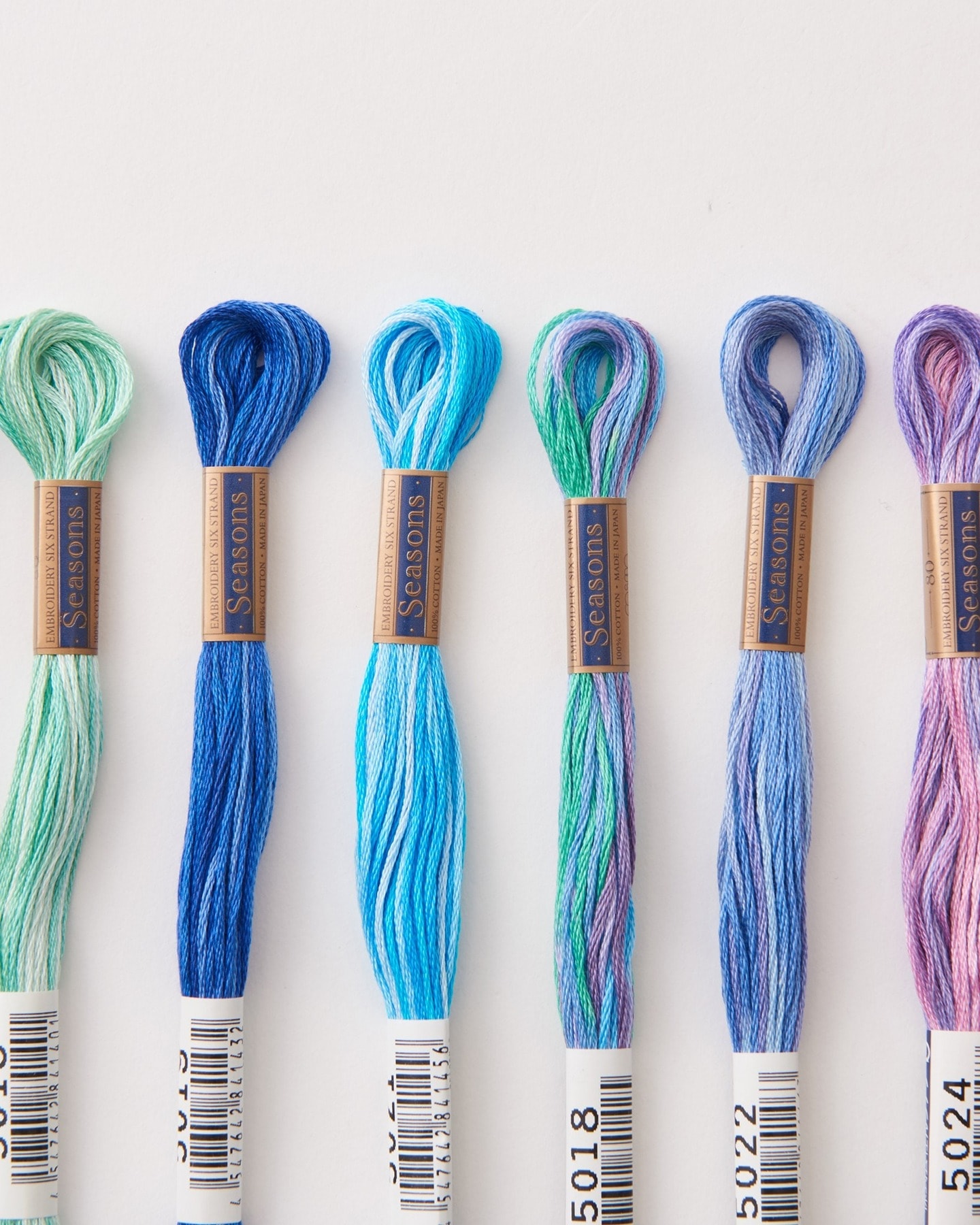 Six COSMO Seasons variegated embroidery floss skeins in cool blue, teal, green, and pink families