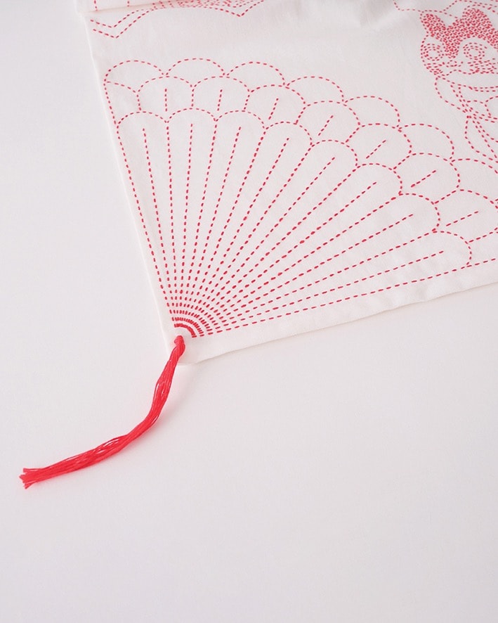 White cloth with red sashiko fan motif and hanging red thread