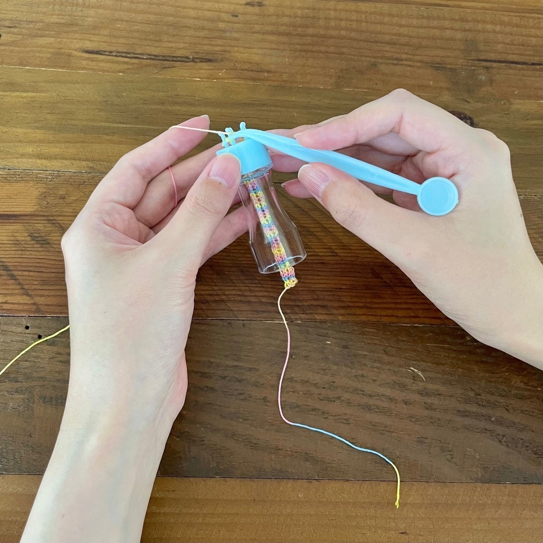 Hands spool-knitting pastel variegated floss into cord with a plastic French knitter