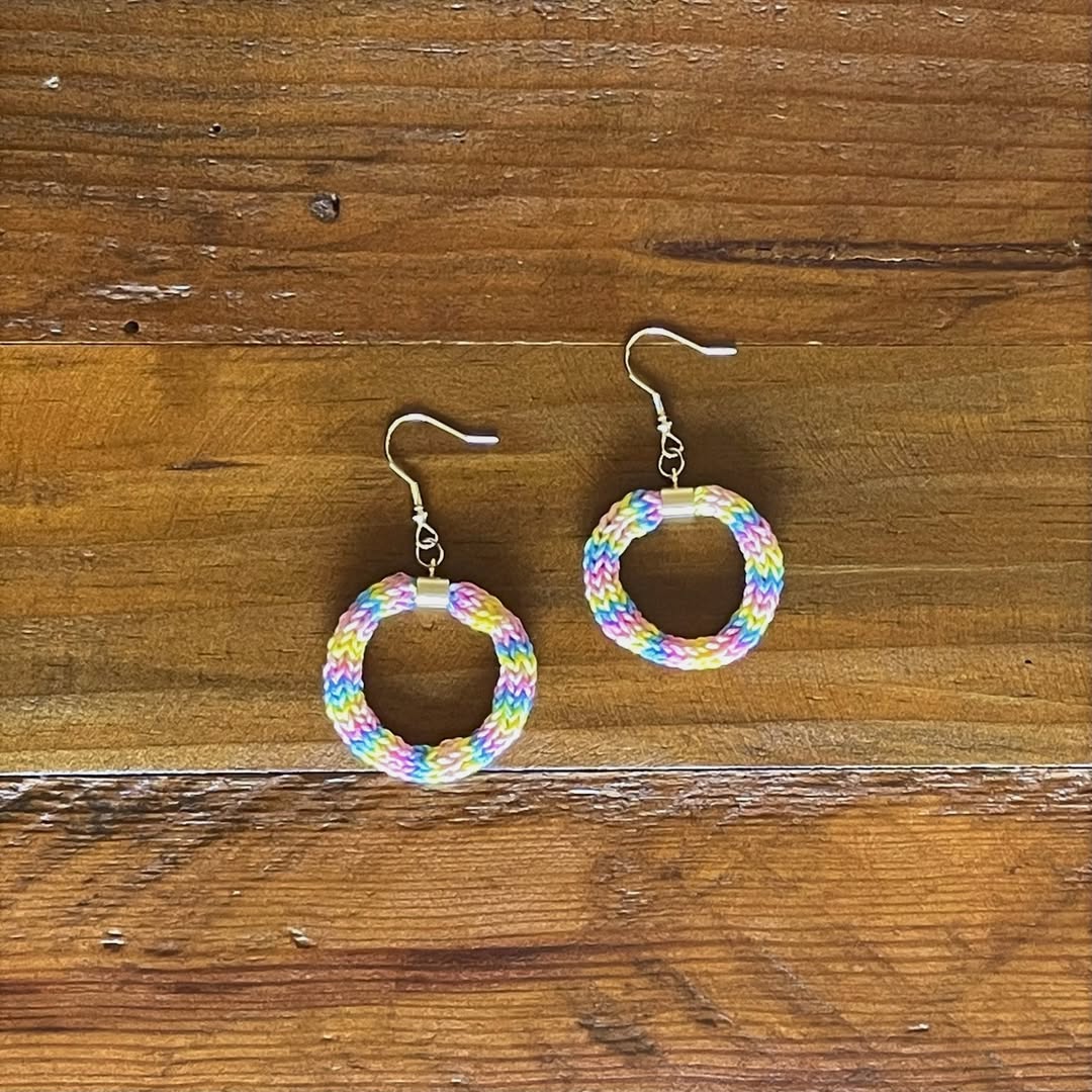 Finished pastel rainbow floss hoop earrings with silver ear wires on wood
