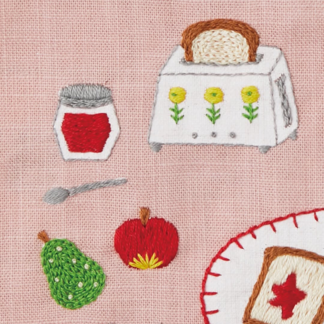Close-up of embroidered toaster, jam jar, and fruit on pink fabric