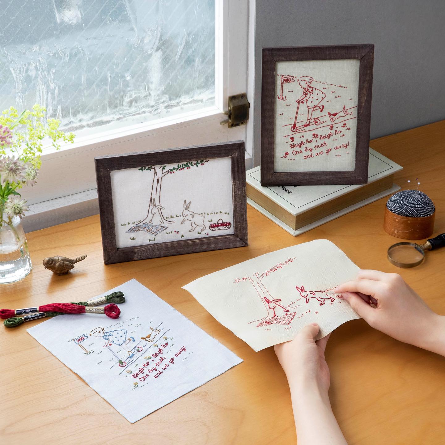 Framed picnic rabbits and scooter motif embroidery by a window with floss and tools