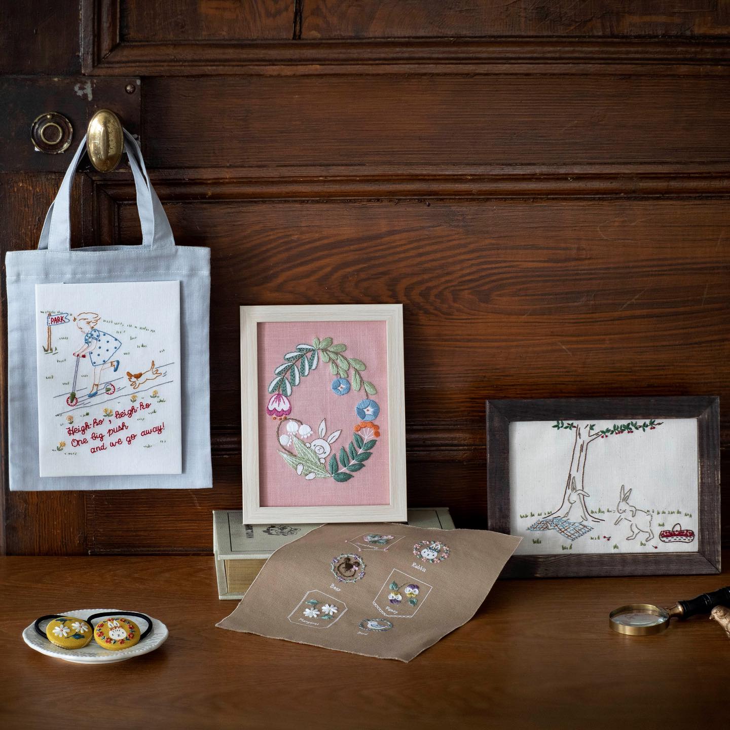 Embroidered tote, framed bunny wreath, picnic rabbits, and small accessories on a wood table