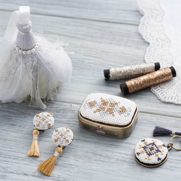 Cross-stitch accessories with gold Nishikiito accents: pill case, earrings, keychain, and tassel doll
