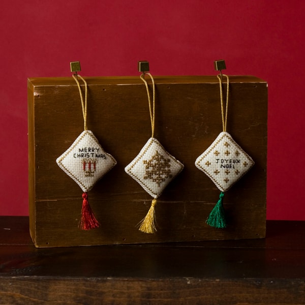 Three cross-stitch Christmas ornaments with gold Nishikiito borders and colorful metallic tassels