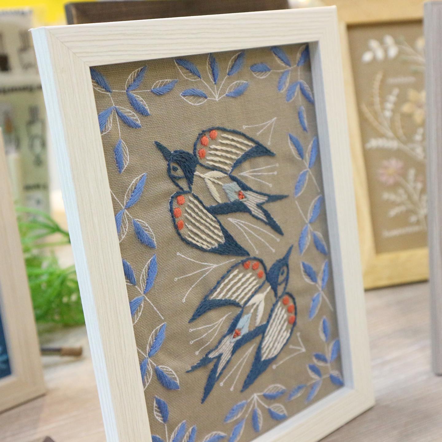 Framed wildflower embroidery sampler grid with botanical motifs on a gallery wall