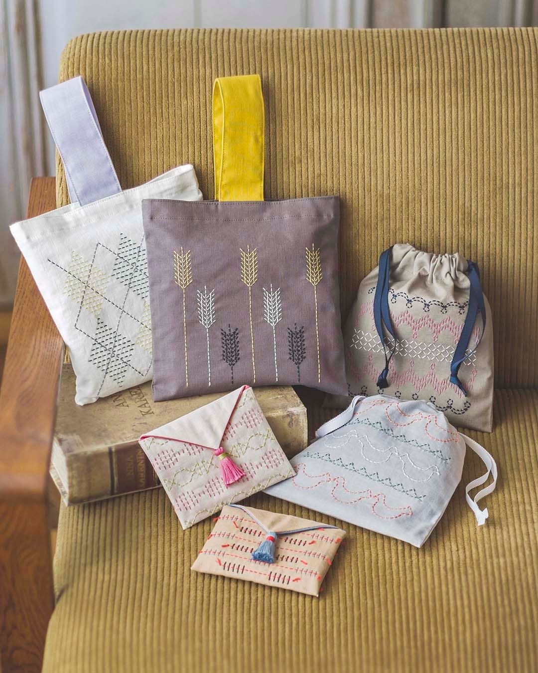 Collection of sashiko-stitched pouches and mini bags arranged on a mustard corduroy chair