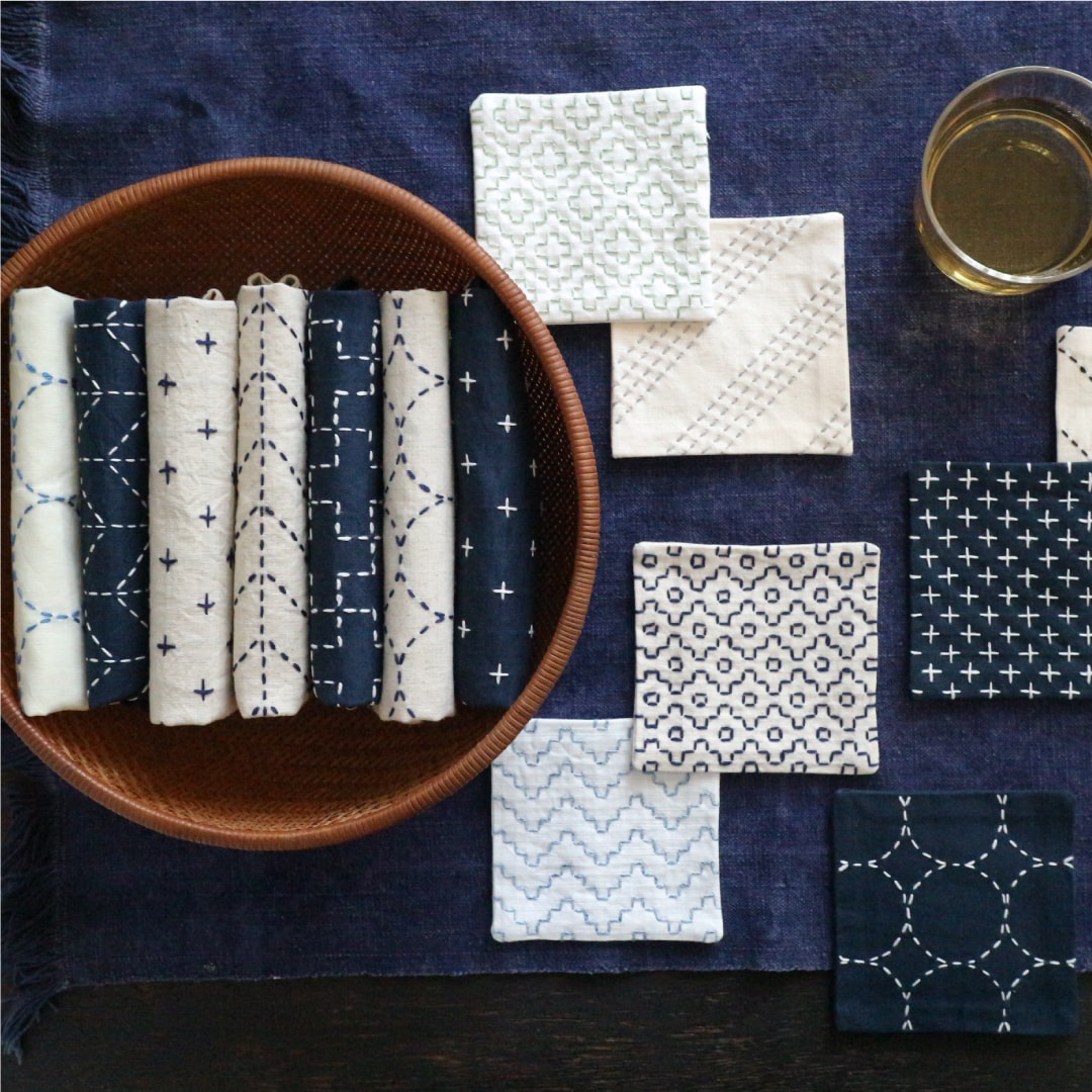 Indigo and cream sashiko coasters and rolled cloths in a basket with tea glass