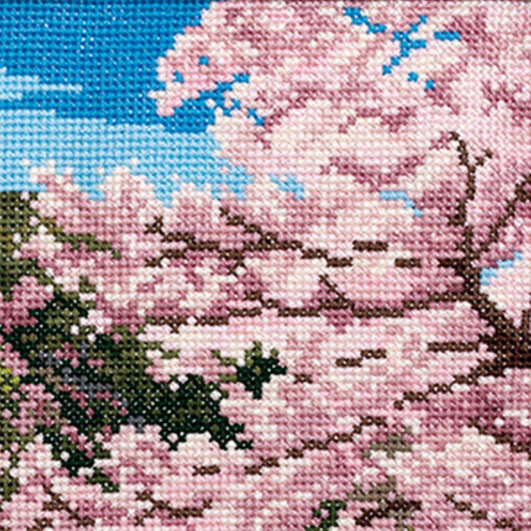 Close-up cross-stitch of cherry blossoms on a branch against a bright blue sky