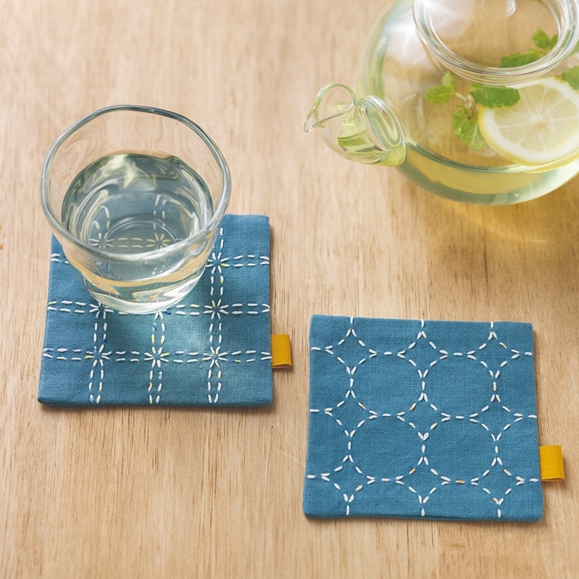 Blue fabric coasters with white sashiko grid and circle patterns beside a teapot