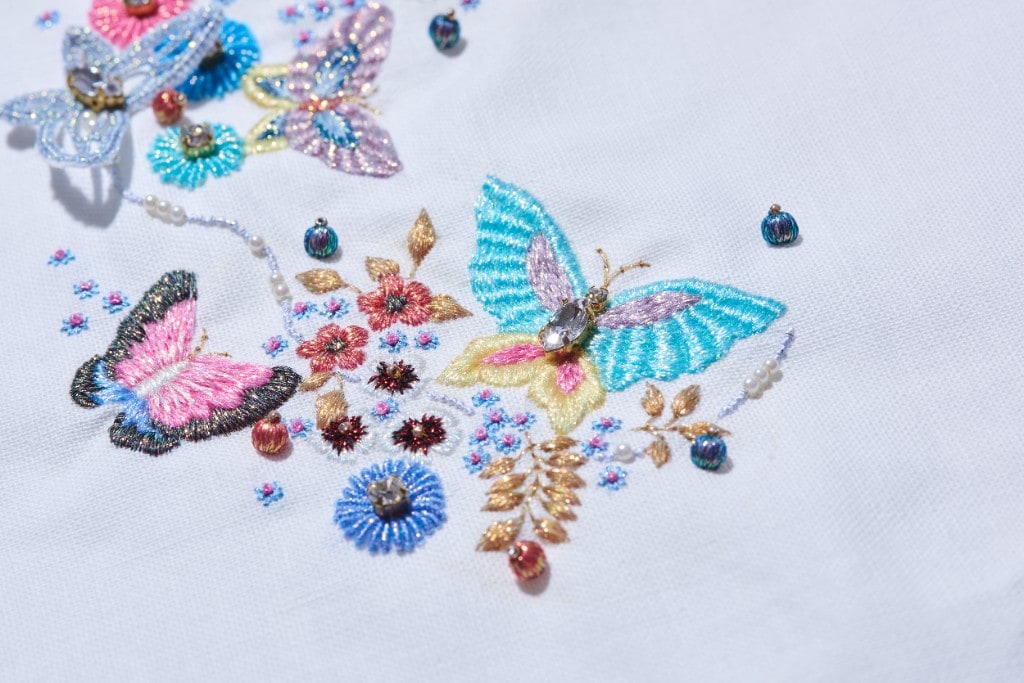 Embroidered butterflies and flowers with beads on white linen, showcasing COSMO thread craftsmanship