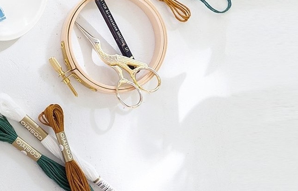 Embroidery hoop, stork scissors, and COSMO floss skeins on a white surface