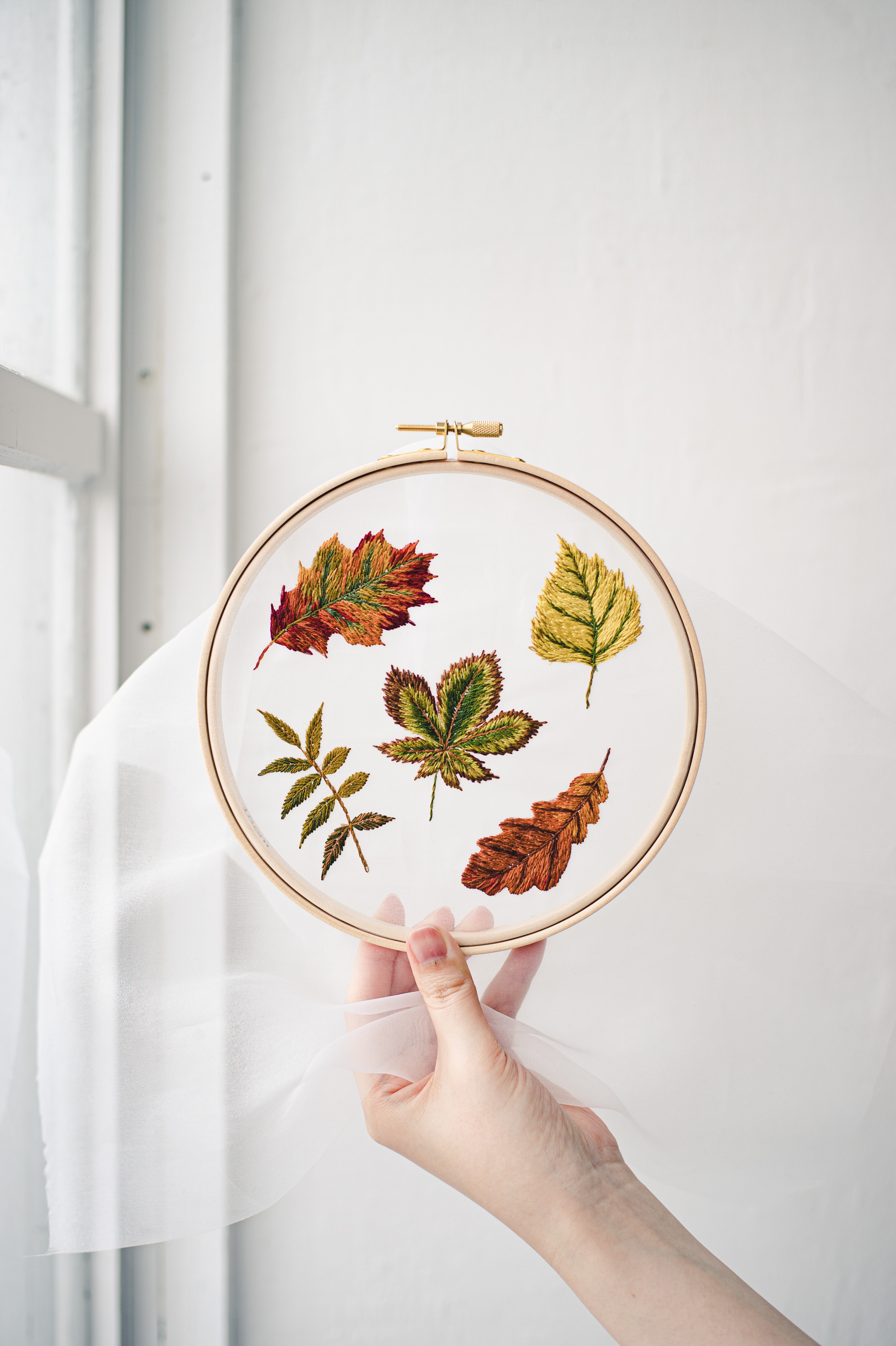 Autumn leaves embroidered in closely matched COSMO floss shades on sheer fabric in a wooden hoop