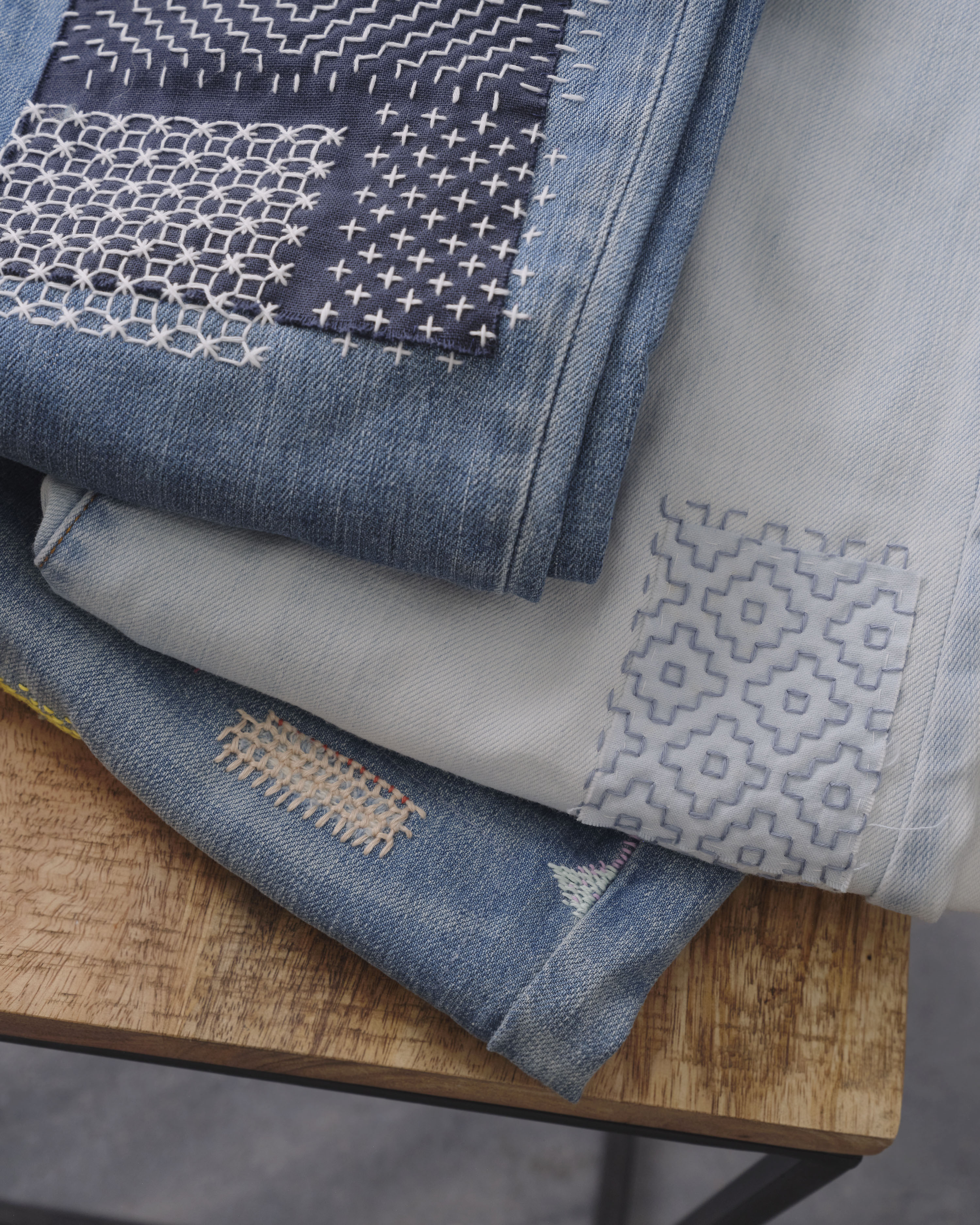 Stack of denim garments repaired with indigo sashiko patches and running stitches