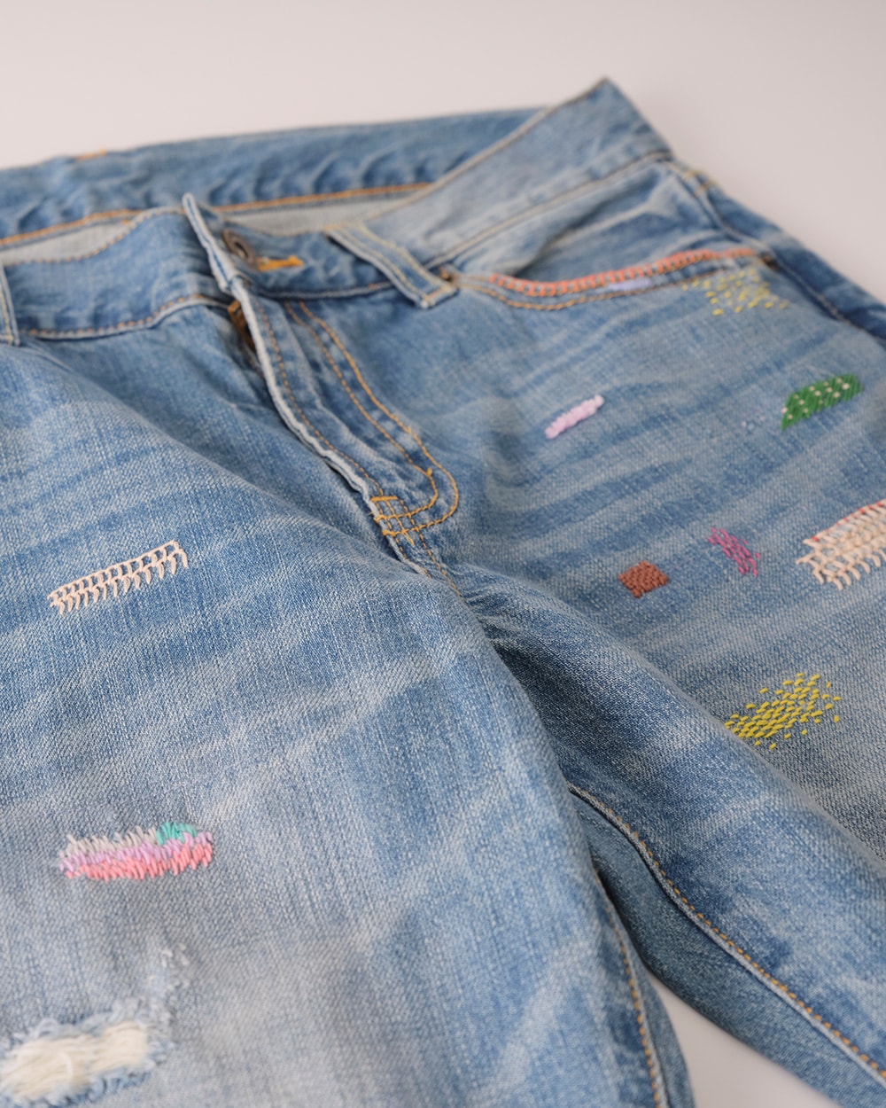 Light-wash denim jeans with colorful visible sashiko mending patches