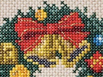 Cross-stitch Christmas wreath detail showing Mirror thread accent on ribbon and bells