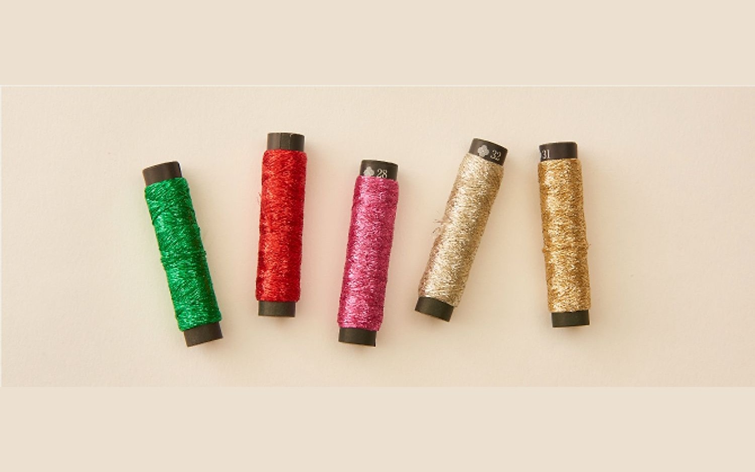 Five spools of COSMO Nishikiito metallic thread in green, red, pink, and gold on a cream background