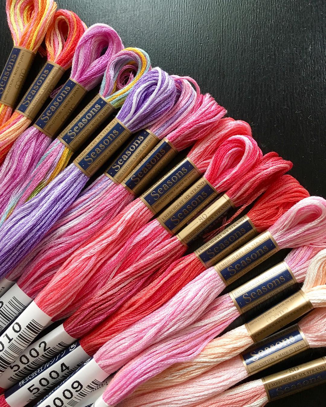 Diagonal arrangement of COSMO Seasons variegated floss skeins in a pink-to-red gradient