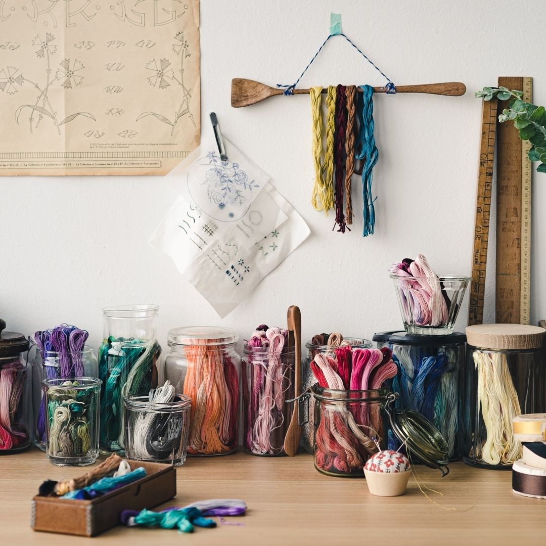 Studio desk with glass jars of COSMO floss sorted by color family and patterns on the wall