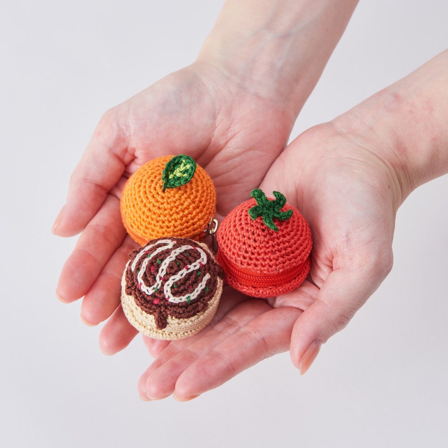 Tomato, orange, and chocolate pouches crocheted with COSMO embroidery floss, held in cupped hands