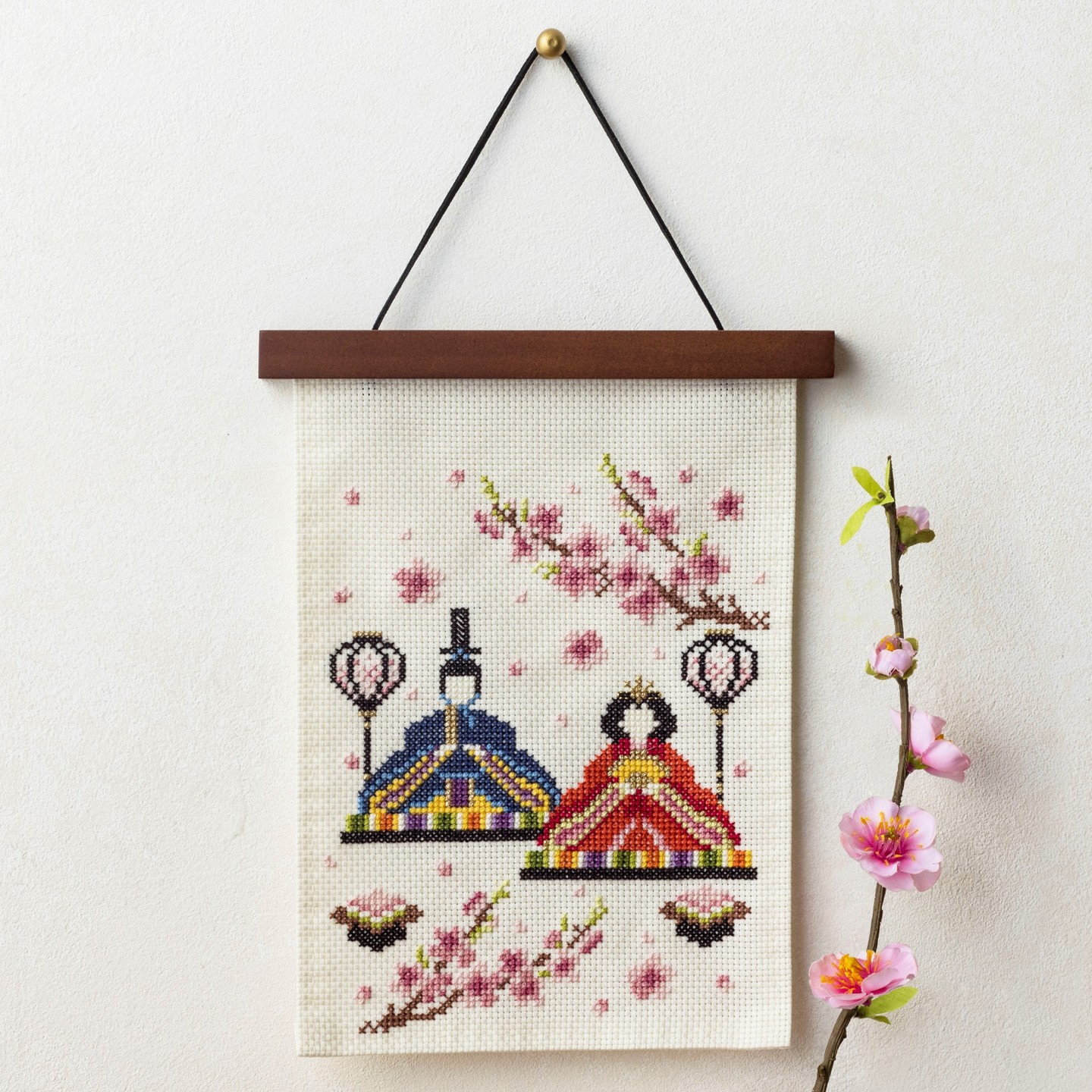 Cross-stitch Hina dolls wall hanging with peach blossoms beside a real blossom branch