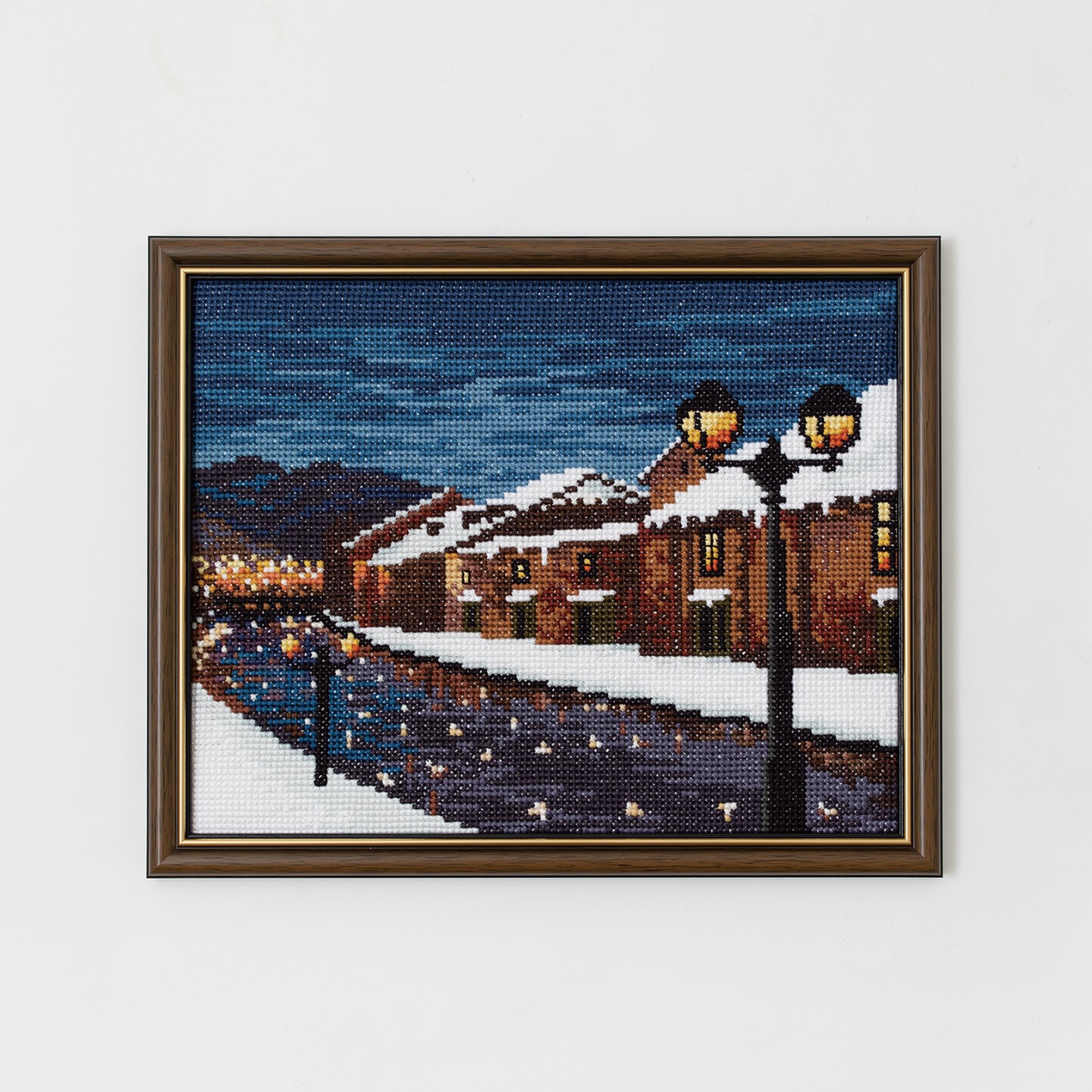 Framed nightscape cross-stitch of a snowy canal with glowing lamps and terracotta buildings