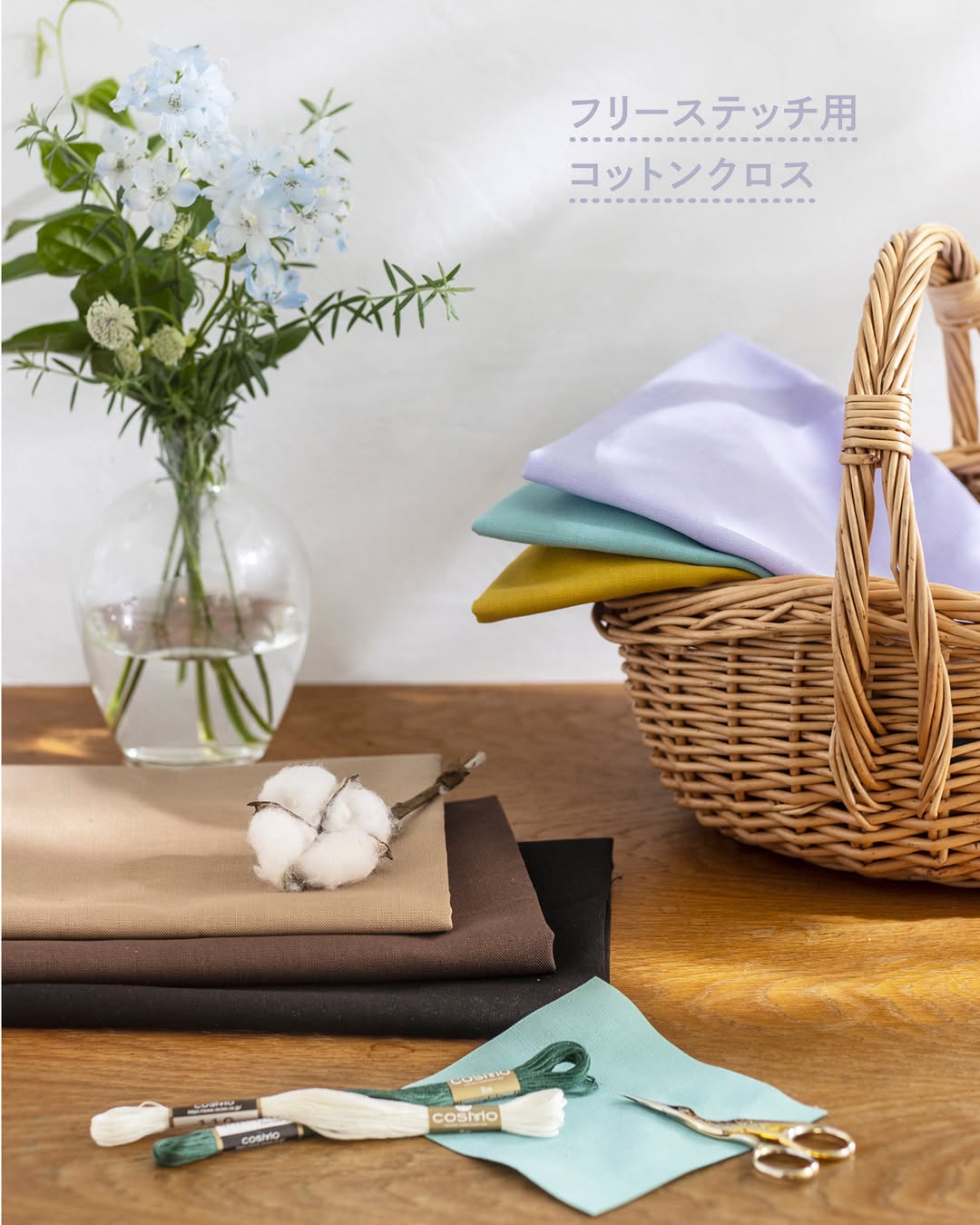COSMO embroidery floss with cotton cloth stacks, gold scissors, and flowers on a wooden table