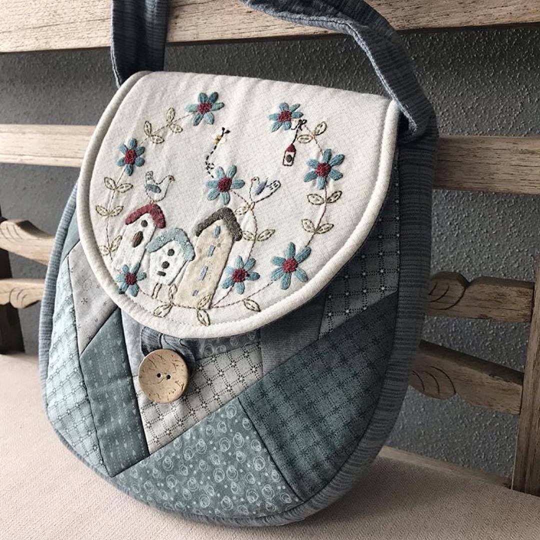 Quilted patchwork shoulder bag with embroidered village scene, birds, and floral wreath
