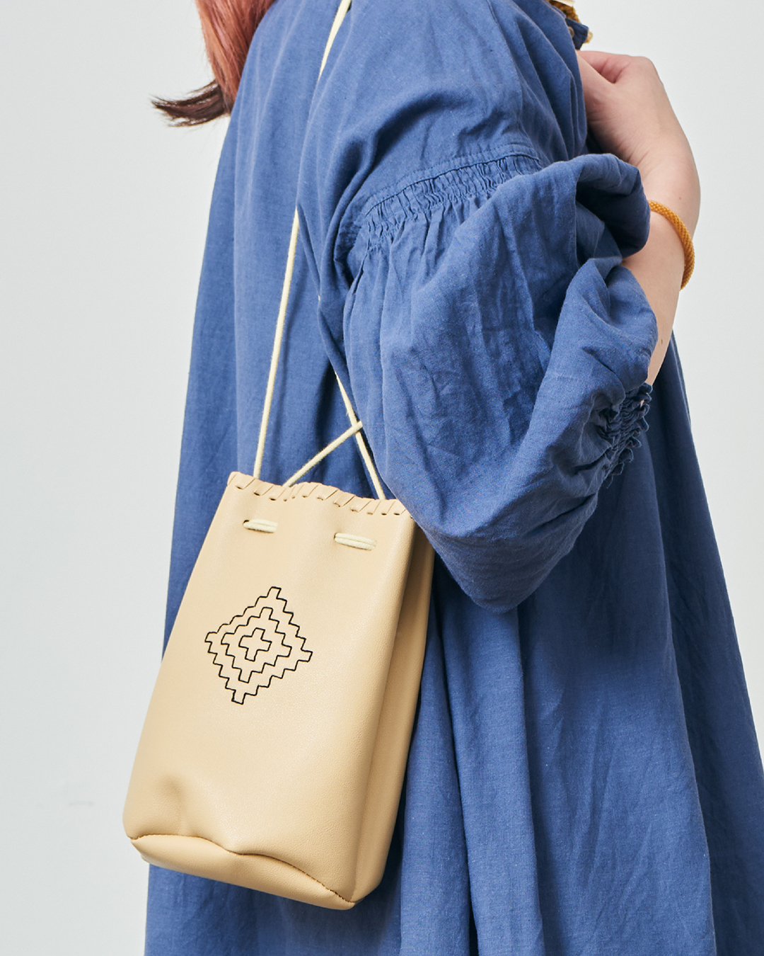 Beige drawstring bag with black diamond geometric embroidery worn over a blue dress